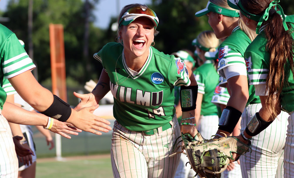 Softball player smiling running and high fiving teammates.