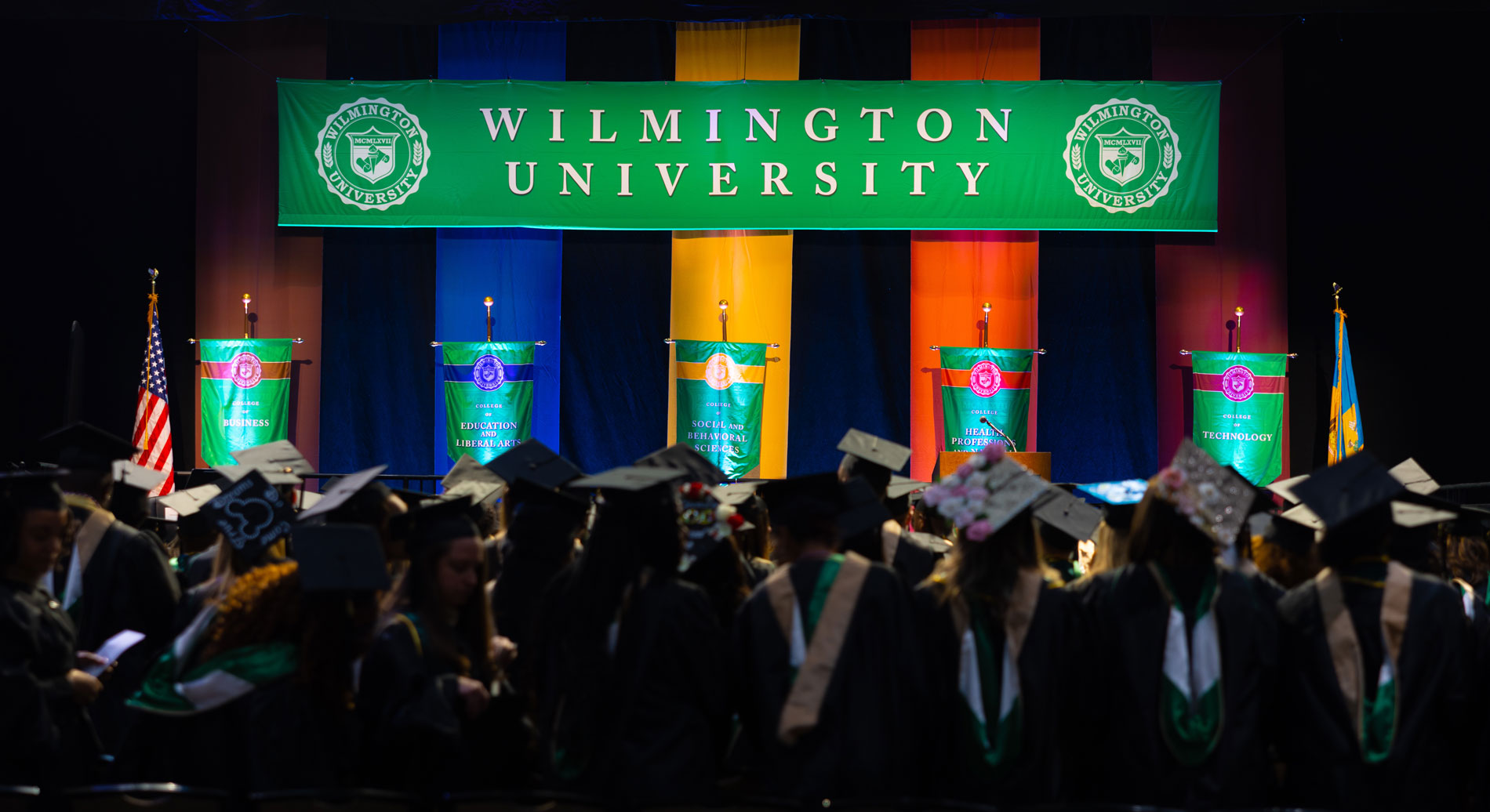 WilmU graduation stage with students gathered in caps and gowns.
