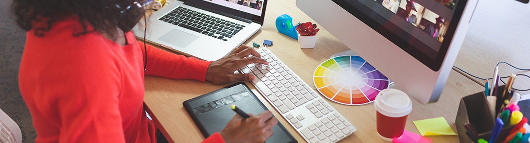 student working on a project  on a computer; surrounded by supplies like: a color wheel, notes, pens, tape, and more