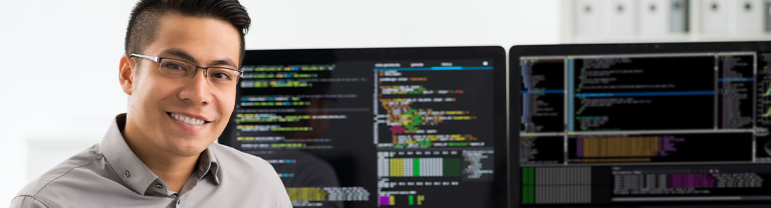 a man sitting in front of two computer screens with coding languages on both screens