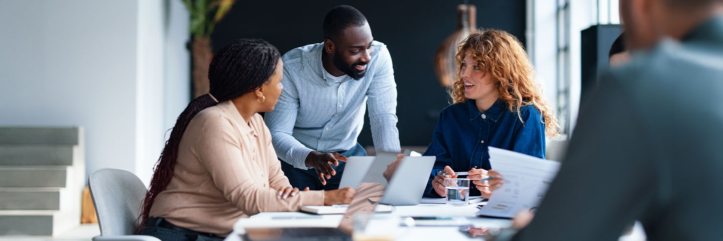 Two women and a man smiling and talking while looking at a laptop in front of them on a desk