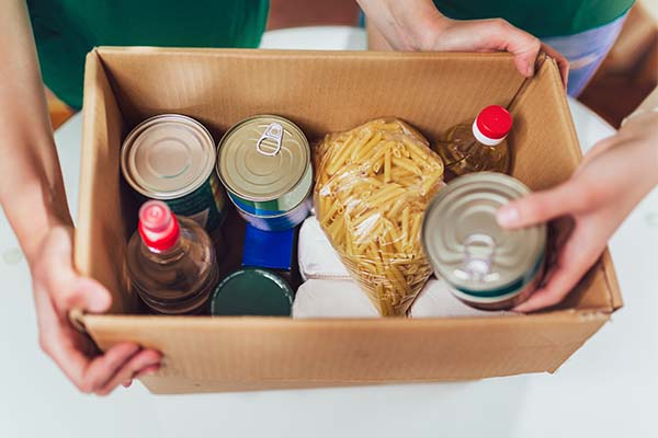 Top view of a cardboard box with foods inside; the box is held by two people