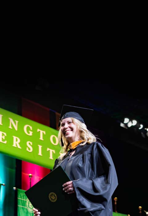 Woman dressed in cap and gown walking across stage with a diploma