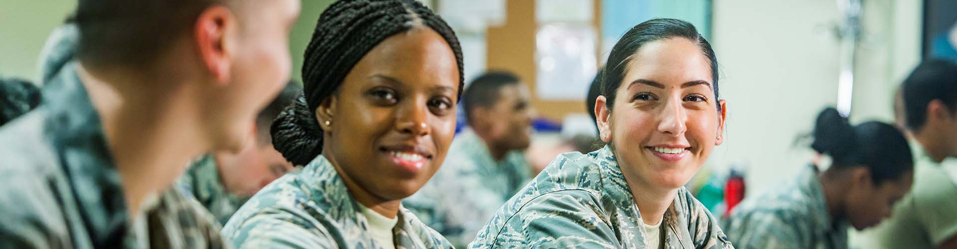 2 women military personnel sitting in class and smiling.