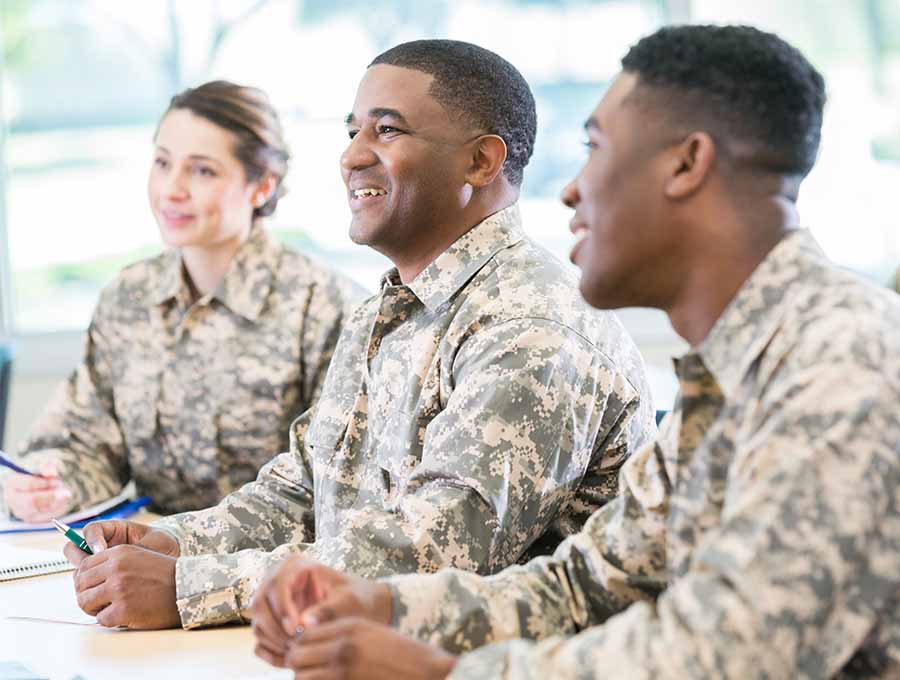 Three military students seated at a table,  listening in class.