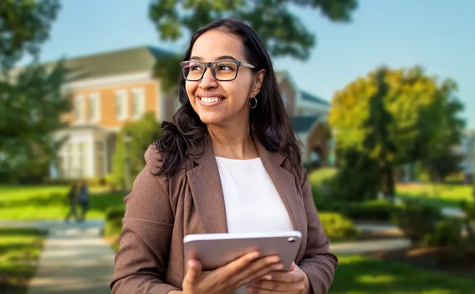 Woman student holding a tablet and smiling while on campus.