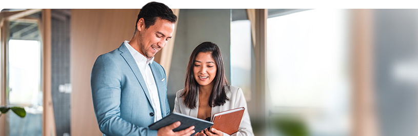 Two dressed in business attire looking at a tablet