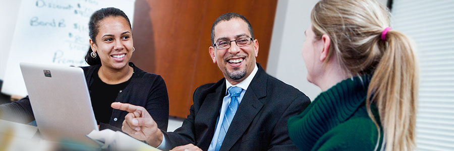 Three people sitting in a conference room, dressed in business attire, smiling